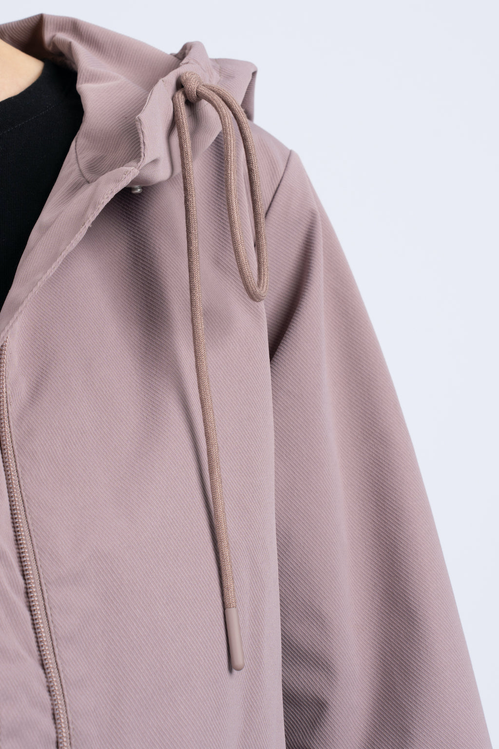 Moteriška pastelinės rožinės spalvos striukė su gobtuvu, reguliuojamu juosmeniu ir užsegamomis kišenėmis, nuotraukoje modelis su striuke, matosi gobtuvo reguliavimo dirželiai