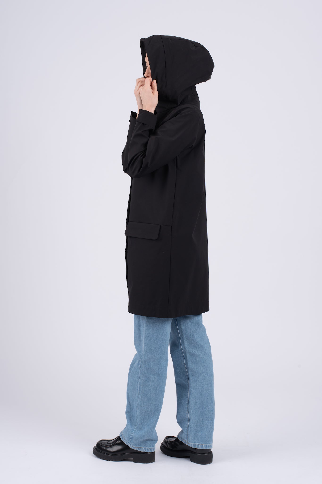 Juoda ilga Elvine moteriška striukė su gobtuvu, užsegama užtrauktuku ir spaudėmis, su kišenėmis priekyje, nuotrauka iš šono, modelis užsidėjęs gobtuvą