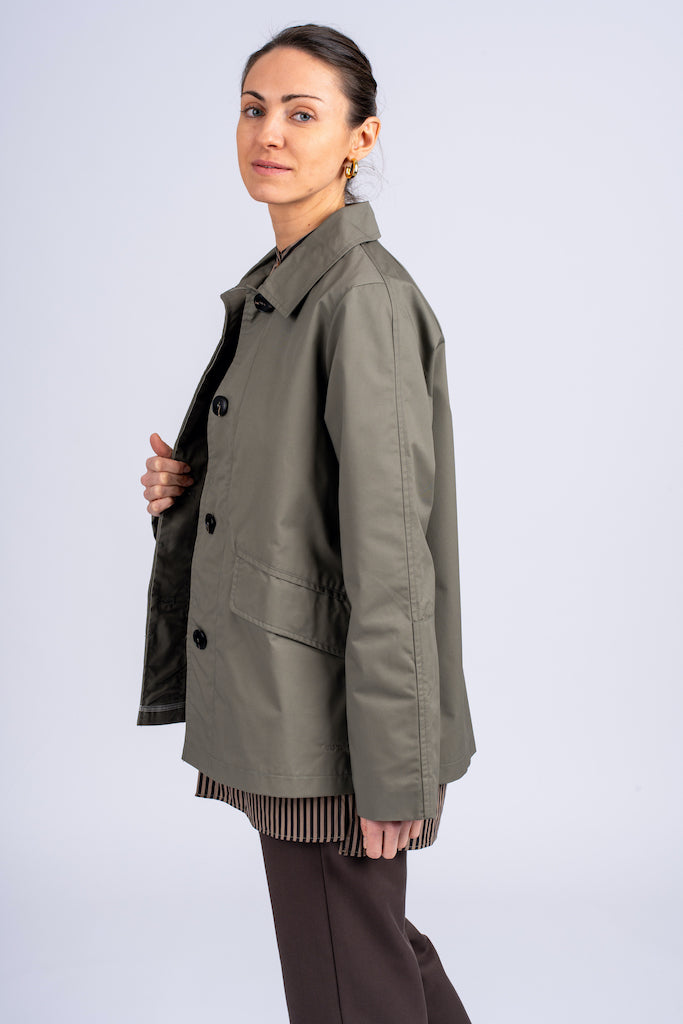 Klasikinis oversized tipo švakelis/striukė pilkos spalvos, vidutinio ilgio, subtiliai maskuoja sėkmenis ir suteikia kasdieniai išvaizdai modernios klasikos įvaizdį, nuotraukoje modelis iš šono, matosi detalė - striukės užsegimas sagomis