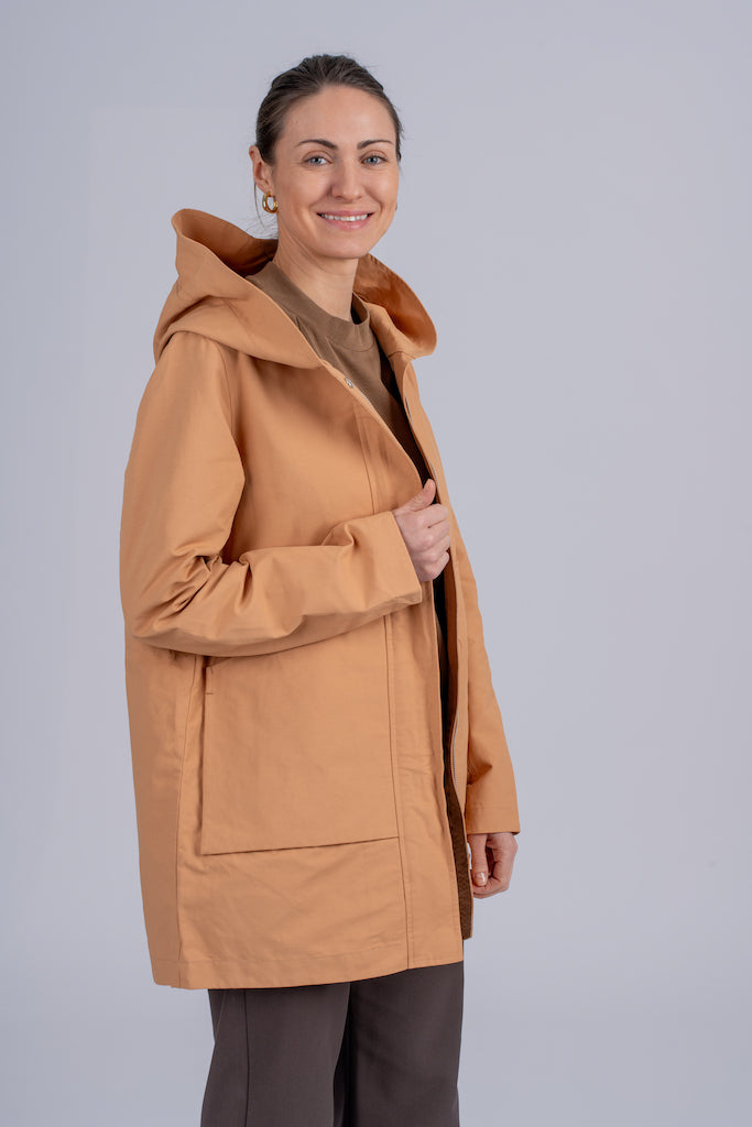 Moteriškas camel spalvos lietpaltis su minimalistiniu dizainu, užtraukiamas užtrauktuku ir dviem kišenėmis, puikiai tinkantis miesto stiliui, nuotraukoje modelis iš šono atsegtu paltu