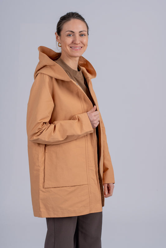 Moteriškas camel spalvos lietpaltis su minimalistiniu dizainu, užtraukiamas užtrauktuku ir dviem kišenėmis, puikiai tinkantis miesto stiliui, nuotraukoje modelis iš šono atsegtu paltu