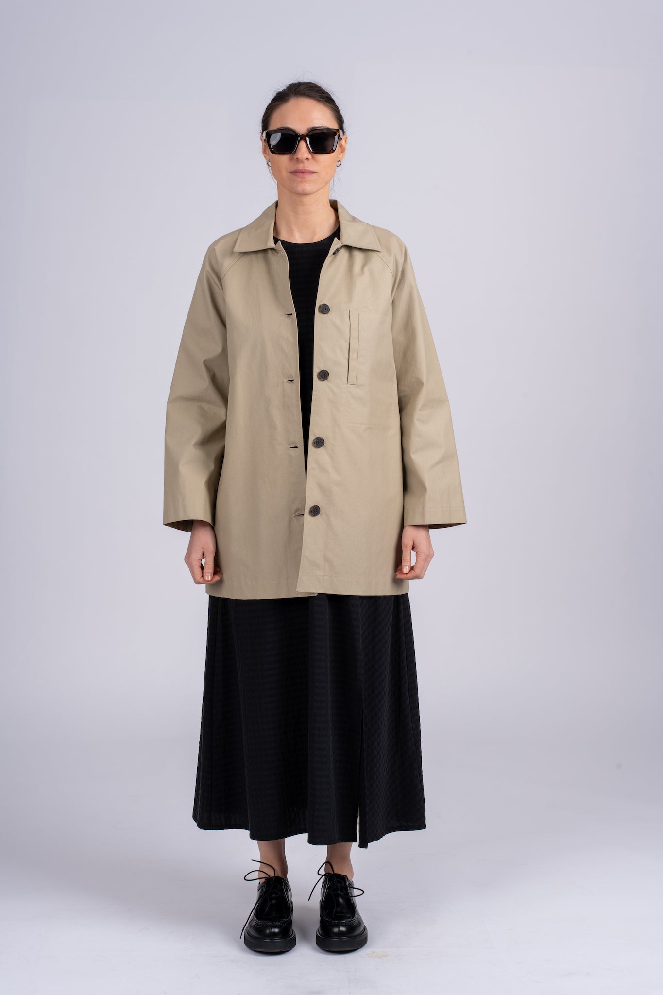 Smėlio spalvos minimalistinio dizaino moteriškas švarkas/striukė su juodomis sagomis ir elegantišku tiesiu siluetu, nuotraukoje modelis su atsegtu švarku iš priekio
