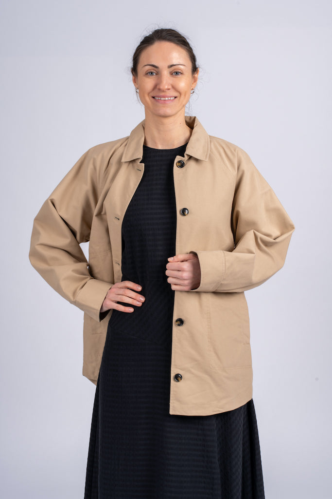 Smėlio spalvos minimalistinio dizaino moteriškas švarkas/striukė su juodomis sagomis ir elegantišku tiesiu siluetu, nuotraukoje modelis su atsegtu švarkeliu