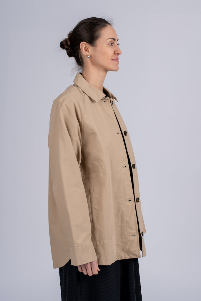 Smėlio spalvos minimalistinio dizaino moteriškas švarkas/striukė su juodomis sagomis ir elegantišku tiesiu siluetu, nuotraukoje modelis iš šono
