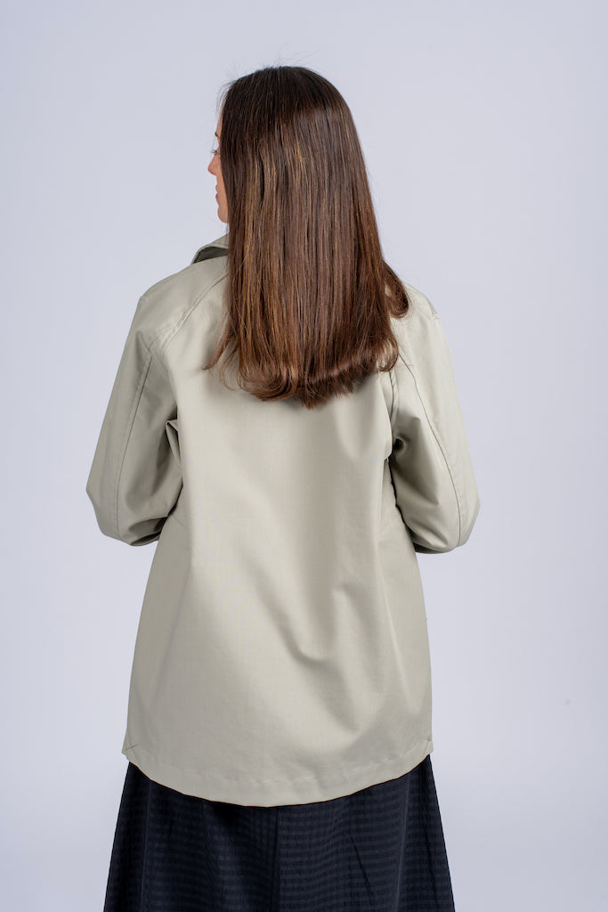 Pastelinės žalios spalvos minimalistinio dizaino moteriškas švarkas/striukė elegantišku tiesiu siluetu, užsagstoma kniedėmis, nuotraukoje modelis su atsegtu švarku iš nugaros