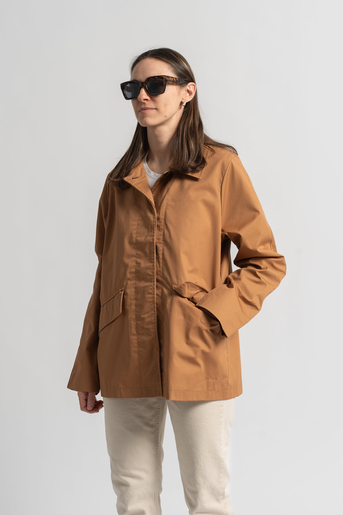Klasikinis oversized tipo švakelis/striukė camel spalvos, vidutinio ilgio, subtiliai maskuoja sėkmenis ir suteikia kasdieniai išvaizdai modernios klasikos įvaizdį, nuotraukoje modelis iš priekio, matosi detalė - magnetu užsegama kišenė priekyje